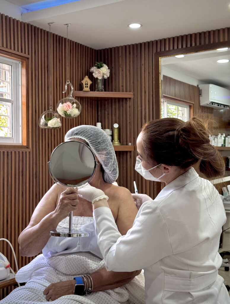 dra-carmen-rosa-guzman-evaluacion-pretratamiento-espejo-estetica-santiago-republica-dominicana Dra. Carmen Rosa Guzmán en consulta de evaluación pretratamiento con paciente frente a un espejo en Santiago, República Dominicana.